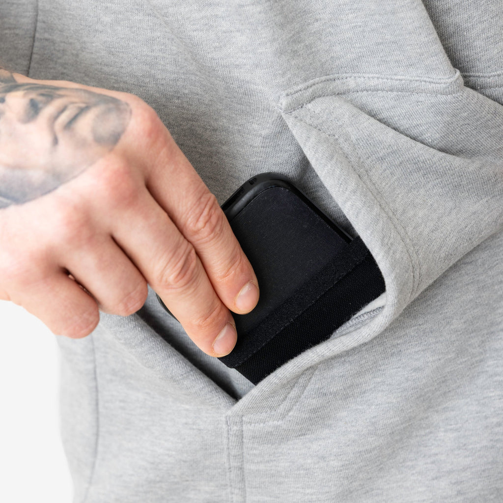 Front of hand pocket with man putting phone in tech pocket of the BRUNT sleeveless water resistant workwear hoodie in light grey heather