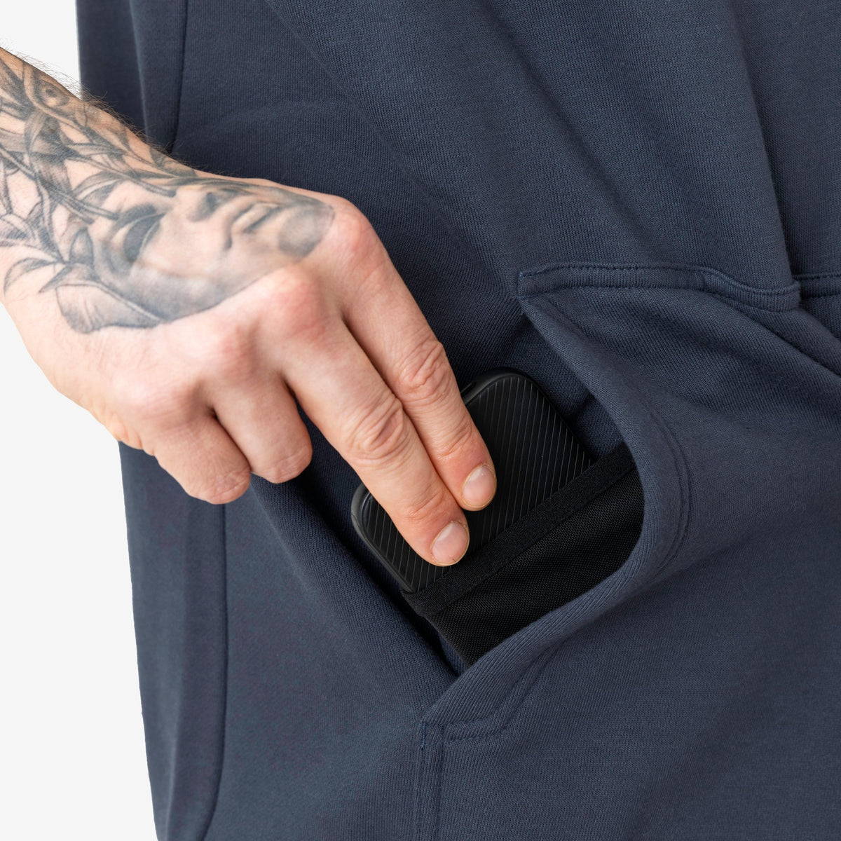Front of hand pocket with man putting phone in tech pocket of the BRUNT sleeveless water resistant workwear hoodie in navy blue