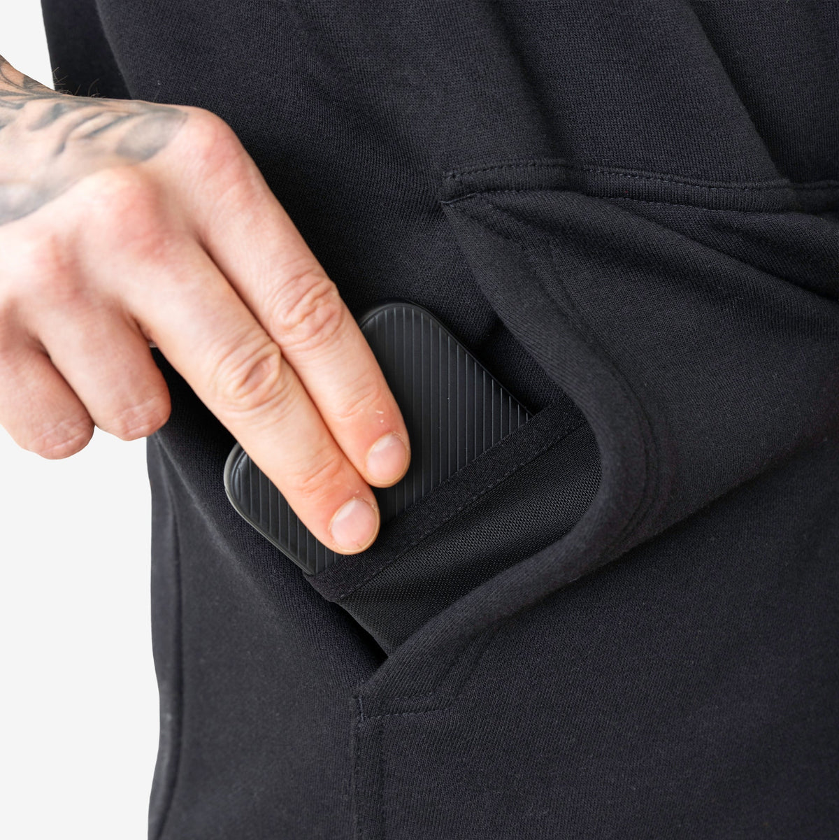 Front of hand pocket with man putting phone in tech pocket of the BRUNT sleeveless water resistant workwear hoodie in black
