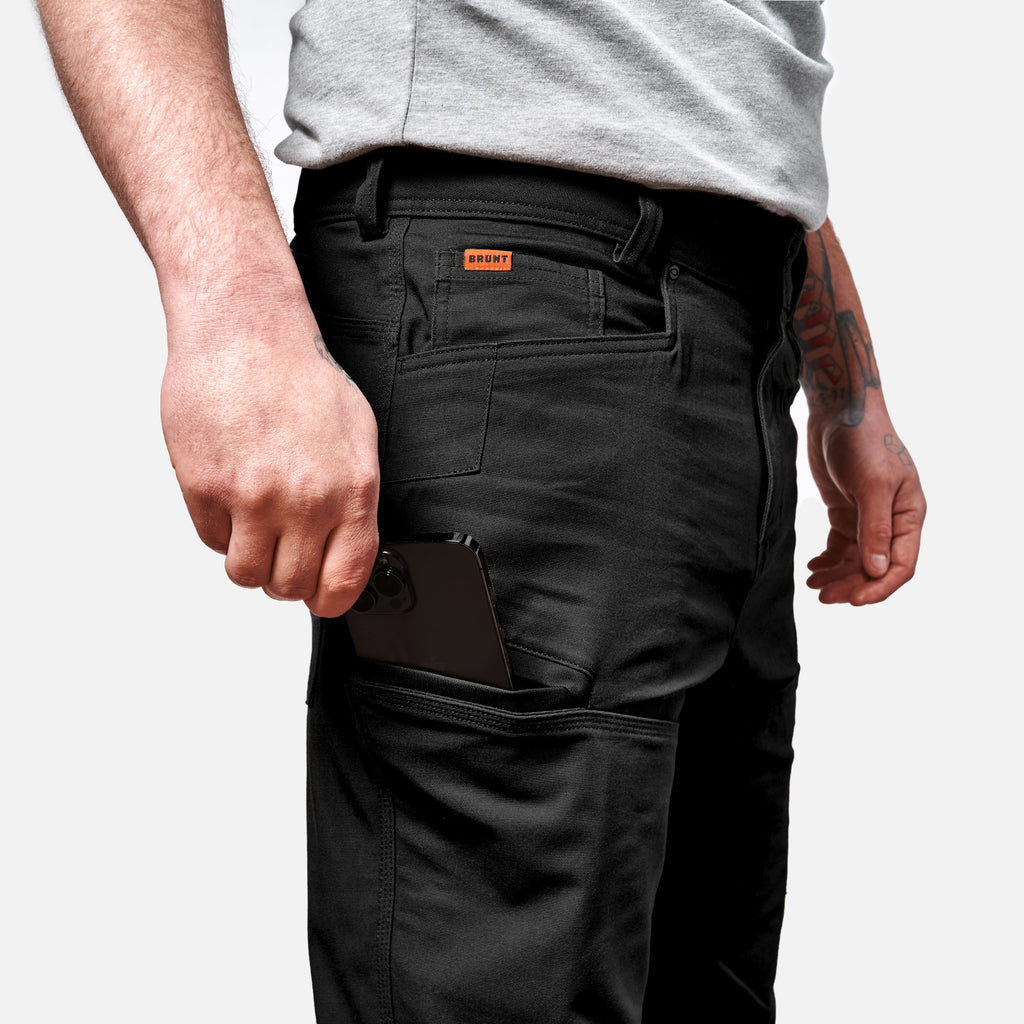 View 2 putting phone in tech pocket of BRUNT water resistant double-knee torra hd work pant in black * 2