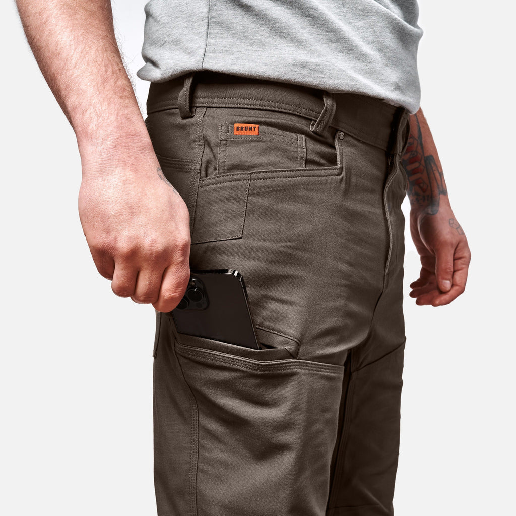 View 2 putting phone in tech pocket of BRUNT water resistant double-knee torra hd work pant in brown * 3