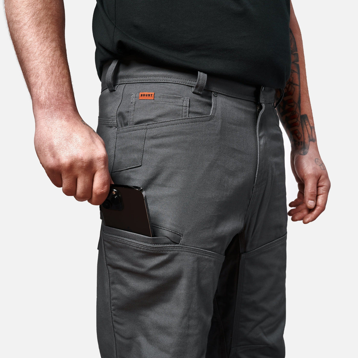 View 2 putting phone in tech pocket of BRUNT water resistant double-knee torra hd work pant in charcoal * 1
