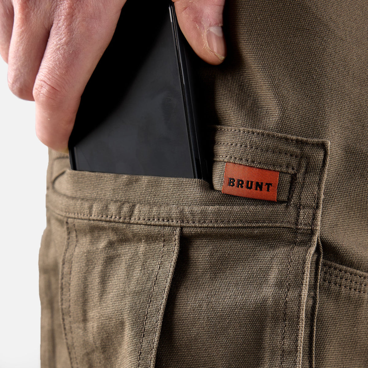 View 2 putting phone in cargo pocket of BRUNT water resistant double knee cargo pants in brown * 2