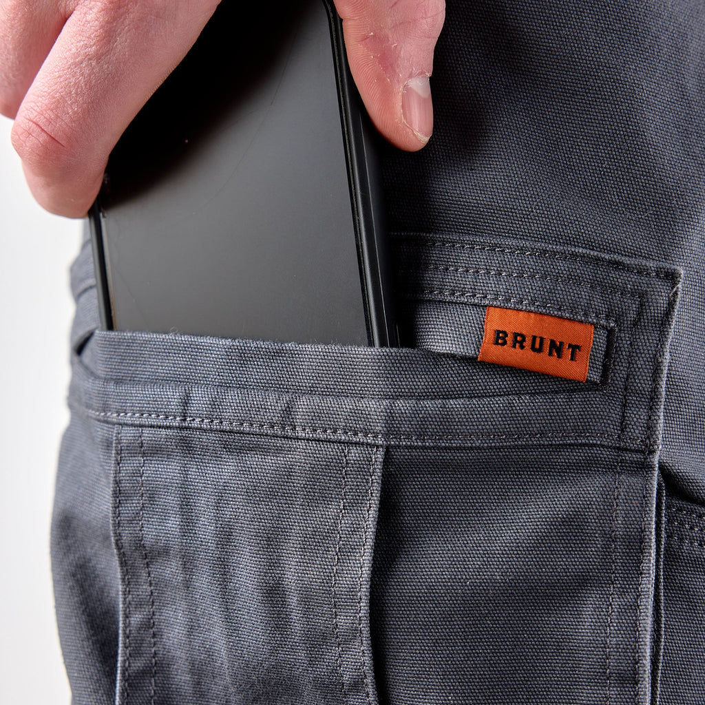 View 2 putting phone in cargo pocket of BRUNT water resistant double knee cargo pants in charcoal * 0