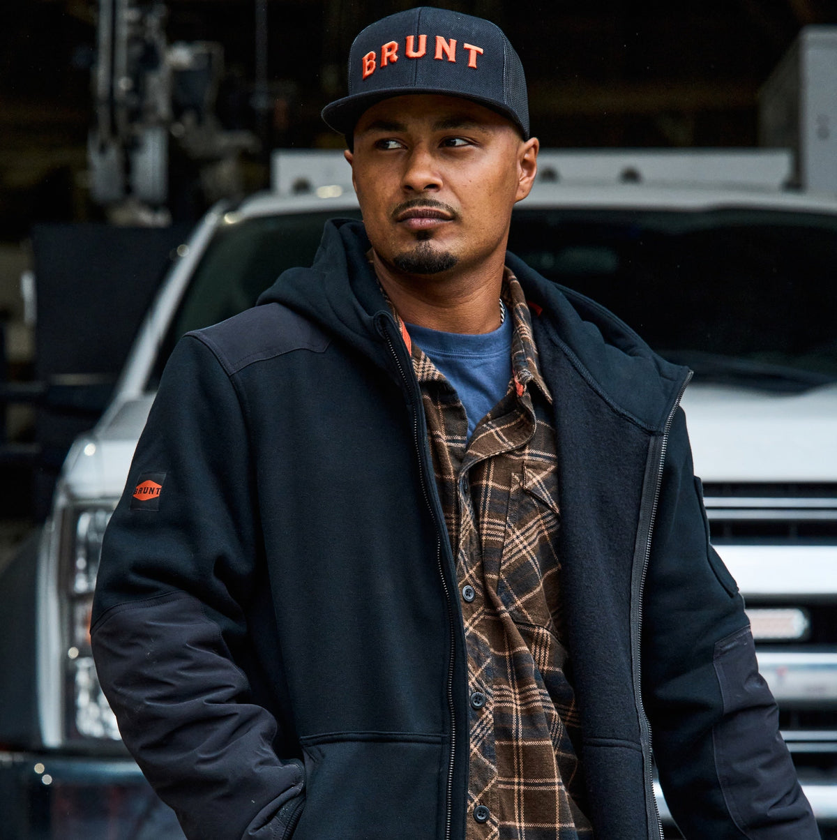 Man on jobsite wearing BRUNT water resistant heavy duty full zip shevlin work hoodie in black