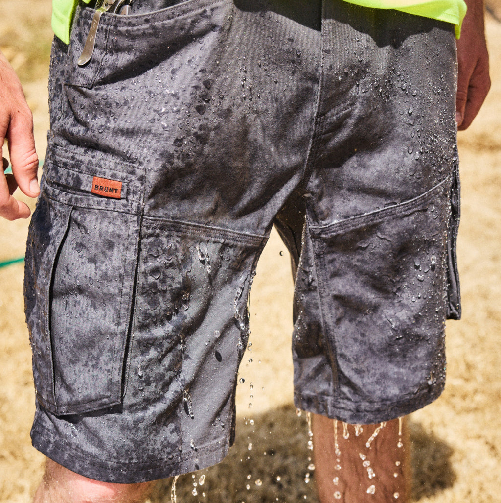 Water rolling off BRUNT abrasion resistant cargo work shorts in charcoal on jobsite
