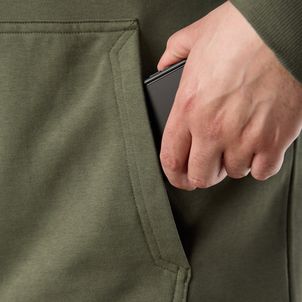 Man putting phone in oversized front pocket of BRUNT comfortable all-season levin work hoodie in moss * 1