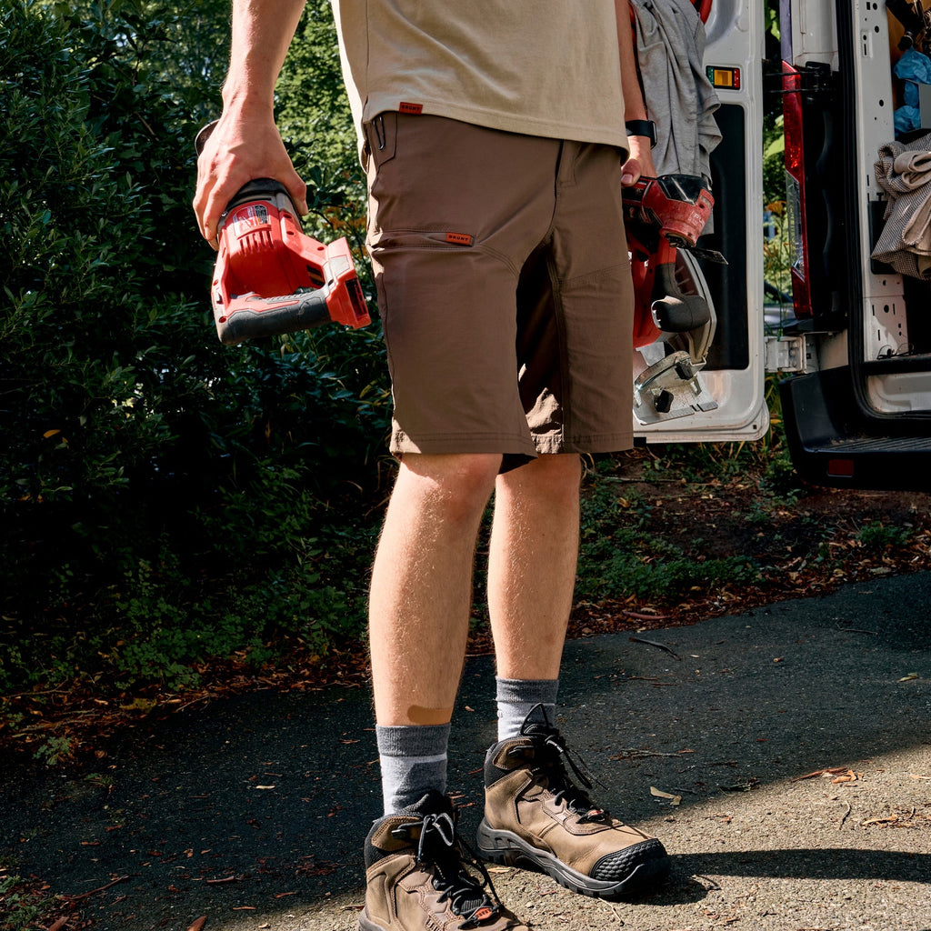 Man on jobsite wearing BRUNT 11 inch lightweight breathable costello work shorts in brown