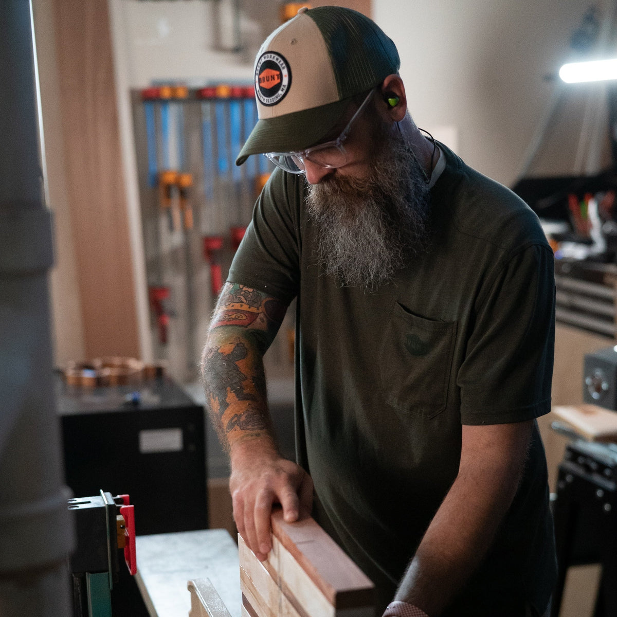 Man wearing curved brim work hats with built in pencil holder and BRUNT logo in army green while using table saw
