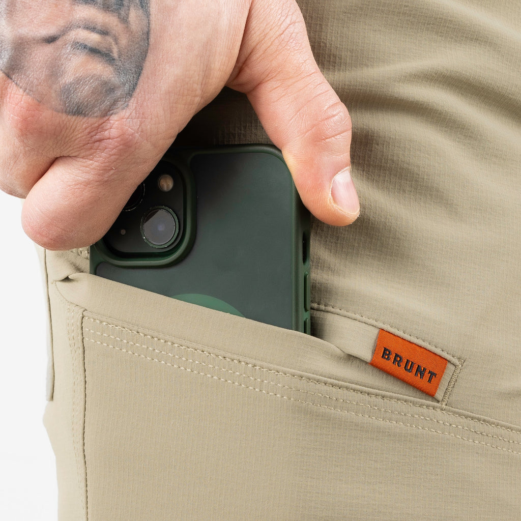 Putting phone in tech pocket of BRUNT 11 inch lightweight breathable costello work shorts in khaki
