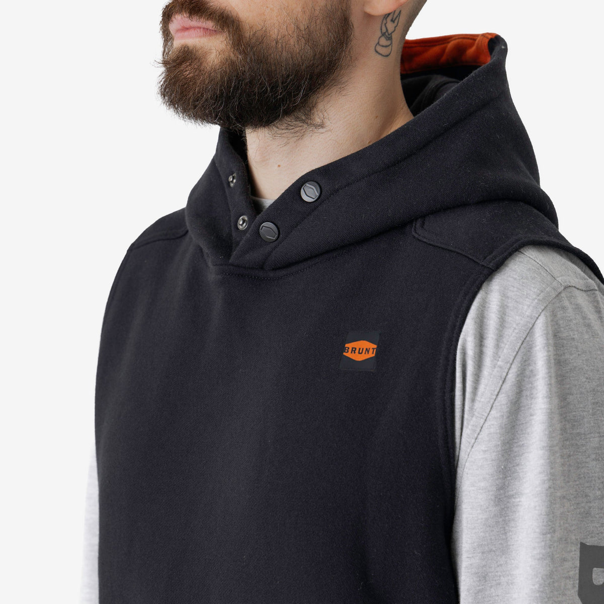 Front of button snaps of the BRUNT sleeveless water resistant workwear hoodie in black with BRUNT high quality long sleeve pocket tee in light grey underneath