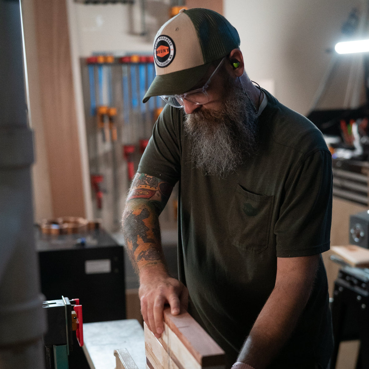 Man wearing curved brim work hats with built in pencil holder and BRUNT logo in army green while using table saw * 4