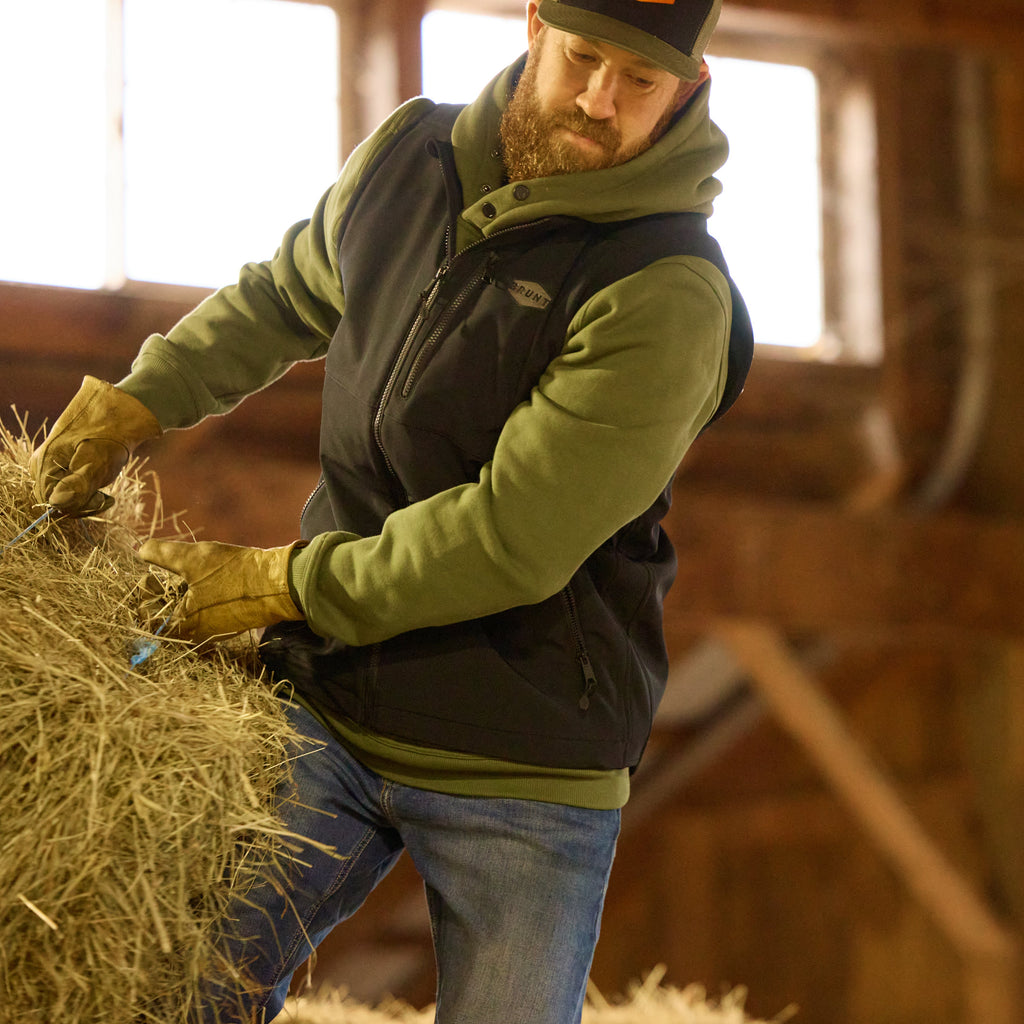 Man wearing front zipper hand pocket of the BRUNT quilted water-resistant work vest in black carrying hay bail